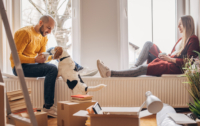 Two people sit by a window enjoying time with pets.