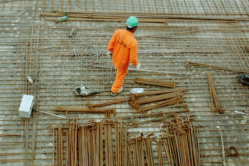 A construction worker in a green hardhat and an orange jumpsuit on the worksite.