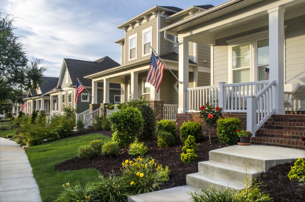 Belmont, North Carolina, USA - June 19, 2016: The American Dream is pictured in this iconic image of the front of a traditional, Victorian-style homes in the Eagle Park neighborhood development. Eagle Park reflects the new style of neighborhoods where homes are built on smaller lots with amenities such as parks, pools and located near small towns and large cities. An American flag hangs from the front porch in celebration to honor an upcoming holiday. Many Americans express patriotism by flying Old Glory, not only on holidays, but all year long. The architecture reflects old styles, however, the construction of the homes has used modern materials and finishes.